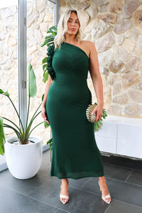 Woman in a green dress standing in front of a stone wall with plants.
