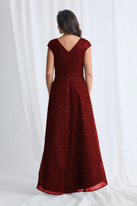 Woman wearing a red evening gown with intricate detailing on a white background