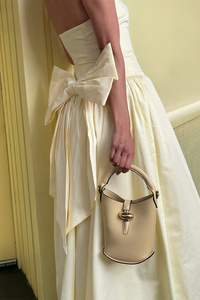 Woman in a white dress holding a matching handbag against a yellow background
