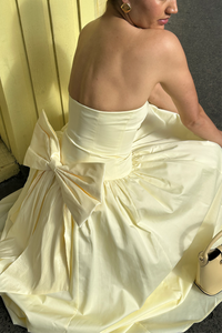 Woman wearing a strapless gown with a large bow detail, sitting against a neutral background.
