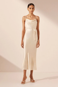 A woman wearing a beige bias cowl midi dress with a silk touch fabric.